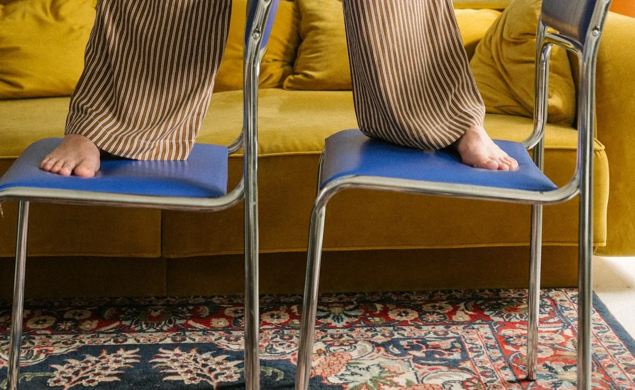Bare feet on two blue chairs in front of a yellow sofa